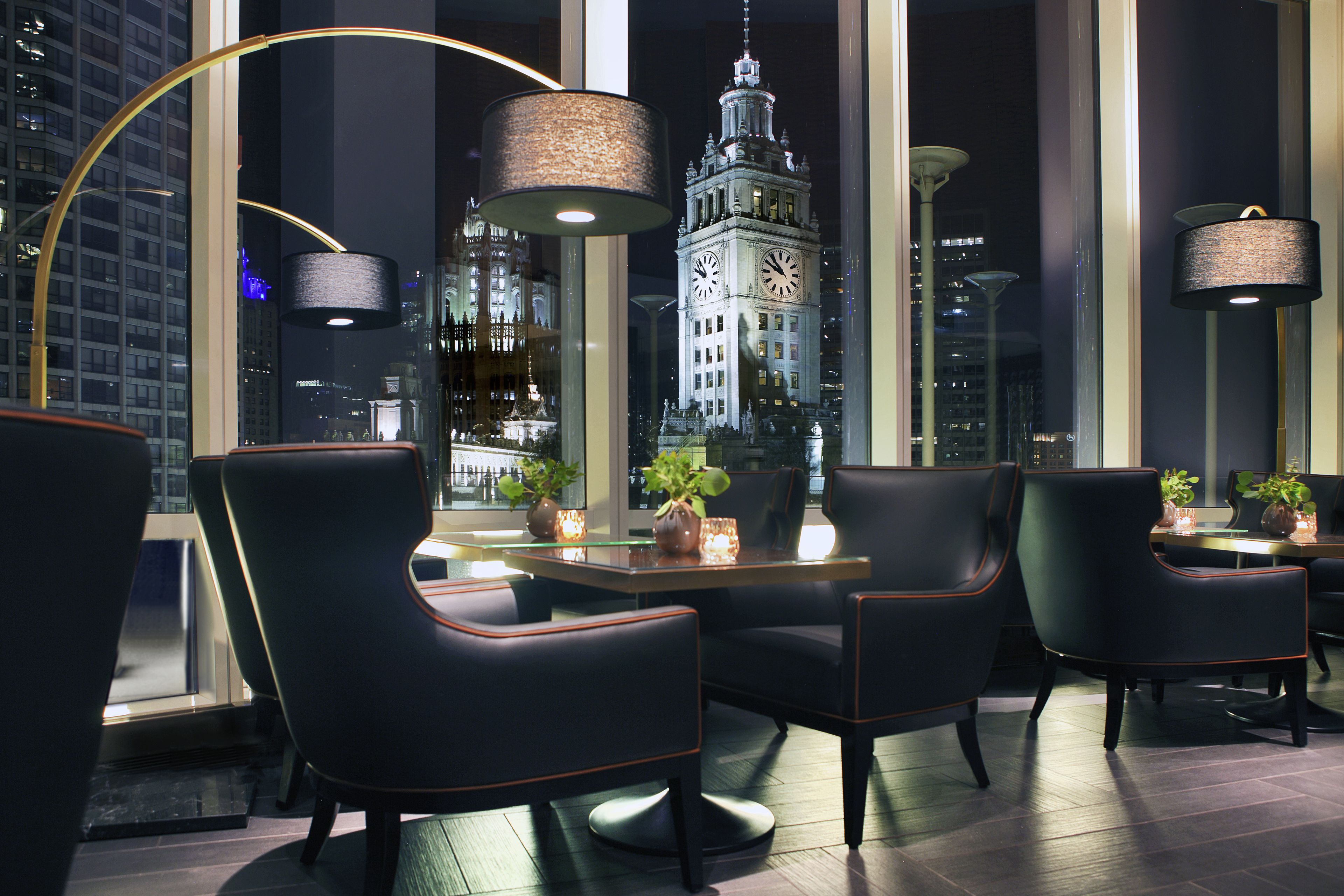 Un comedor moderno con sillas de cuero negro, una mesa redonda y grandes ventanales con vistas a una torre del reloj.