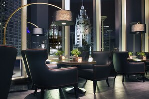 Un espace repas moderne avec des chaises en cuir noir, une table ronde et de grandes fenêtres donnant sur un beffroi.