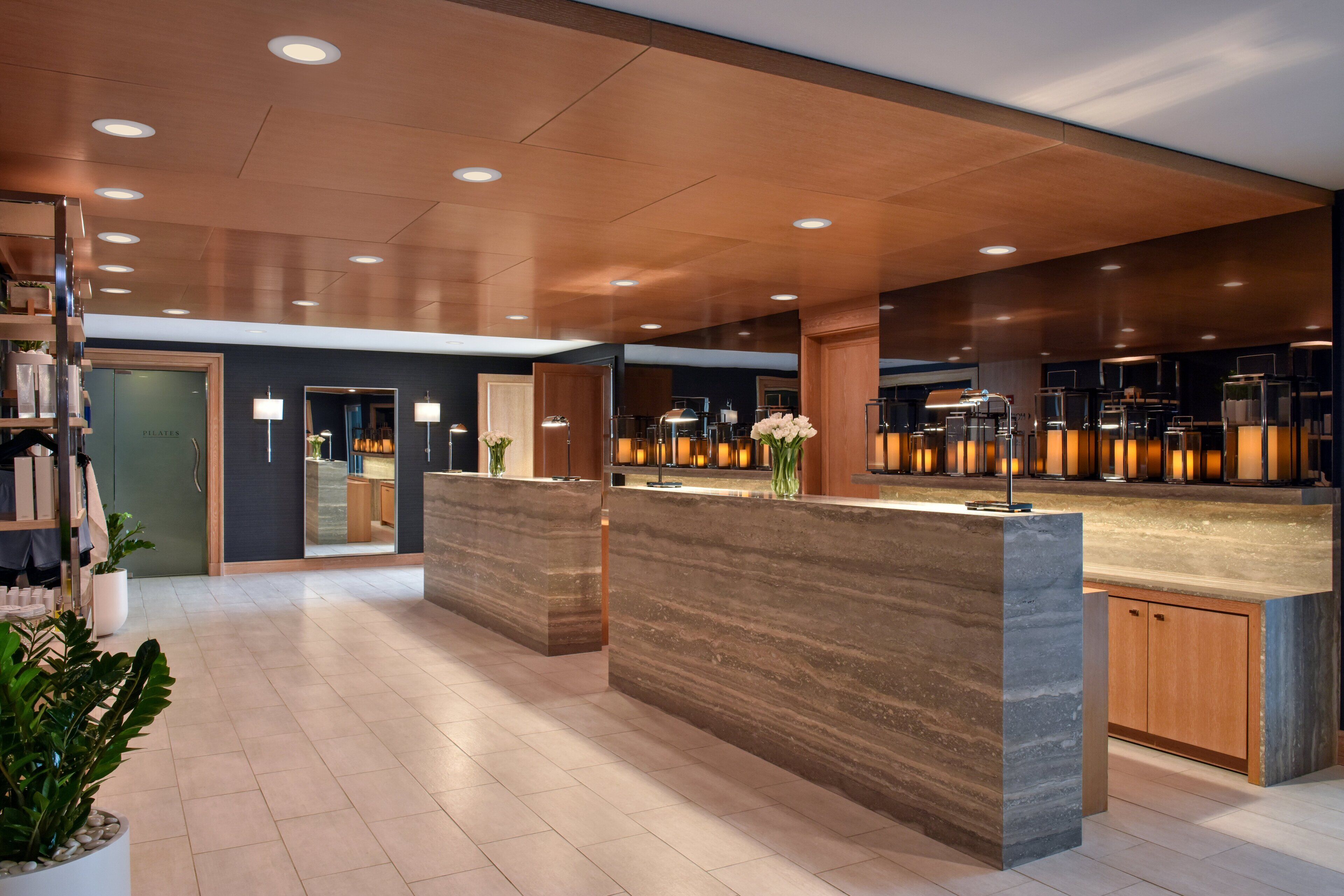 Un hall d’hôtel moderne avec des comptoirs de réception en marbre, des meubles en bois et des plantes en pot.