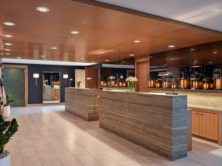 Un hall d’hôtel moderne avec des comptoirs de réception en marbre, des meubles en bois et des plantes en pot.