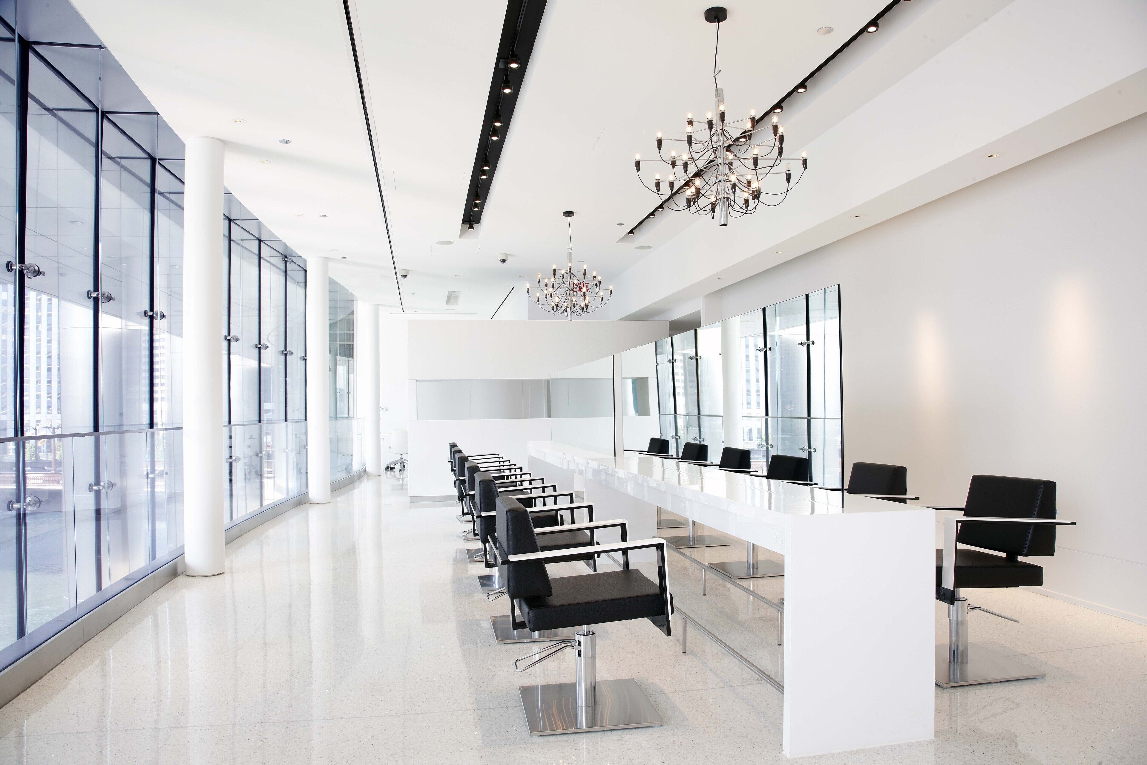 A modern, spacious hotel lobby with a long reception desk, black chairs, and a chandelier.