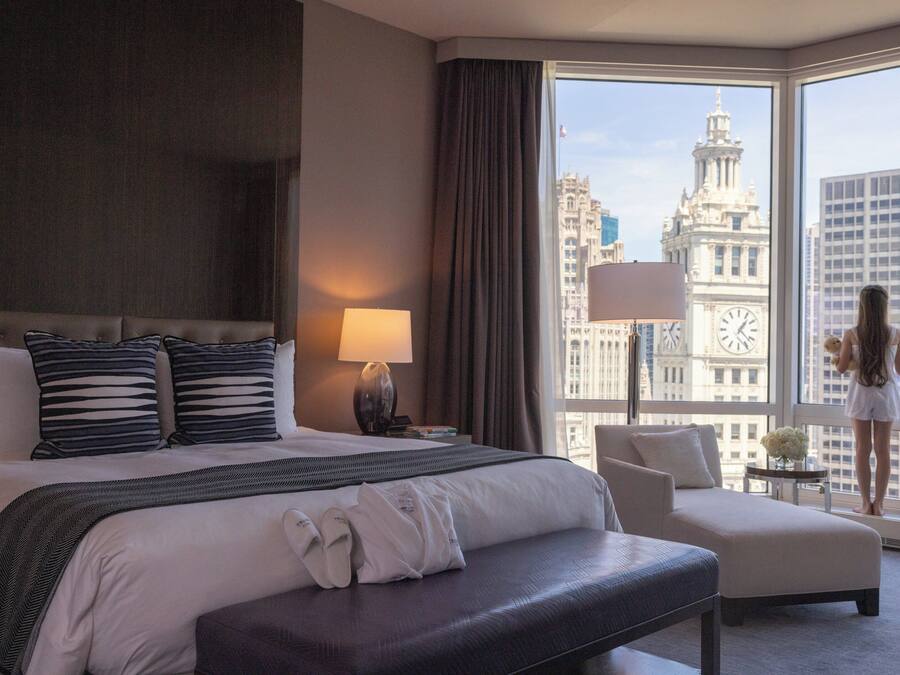 A hotel room with a large bed, a sitting area, and a view of a cityscape including a clock tower.