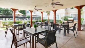 Un patio exterior con mesas y sillas, ventiladores de techo y una parrilla.