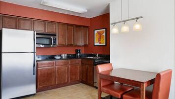 A compact kitchen with wooden cabinets, a stainless steel refrigerator, a microwave, and a dishwasher. There is a dining table with two chairs.