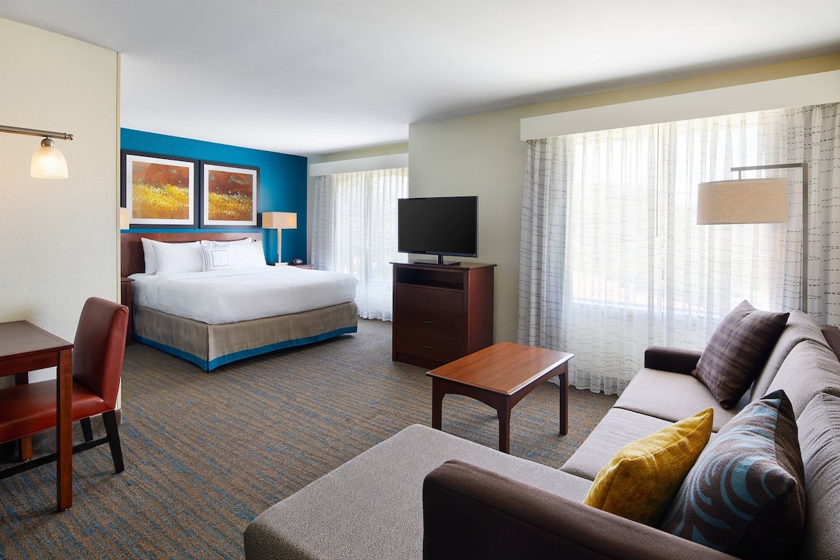 A hotel room with a bed, a sofa, a desk, and a TV.