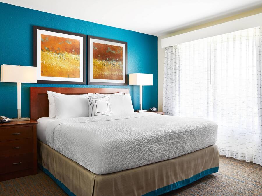 A hotel room with a large bed, two bedside lamps, a nightstand, and artwork on the wall.