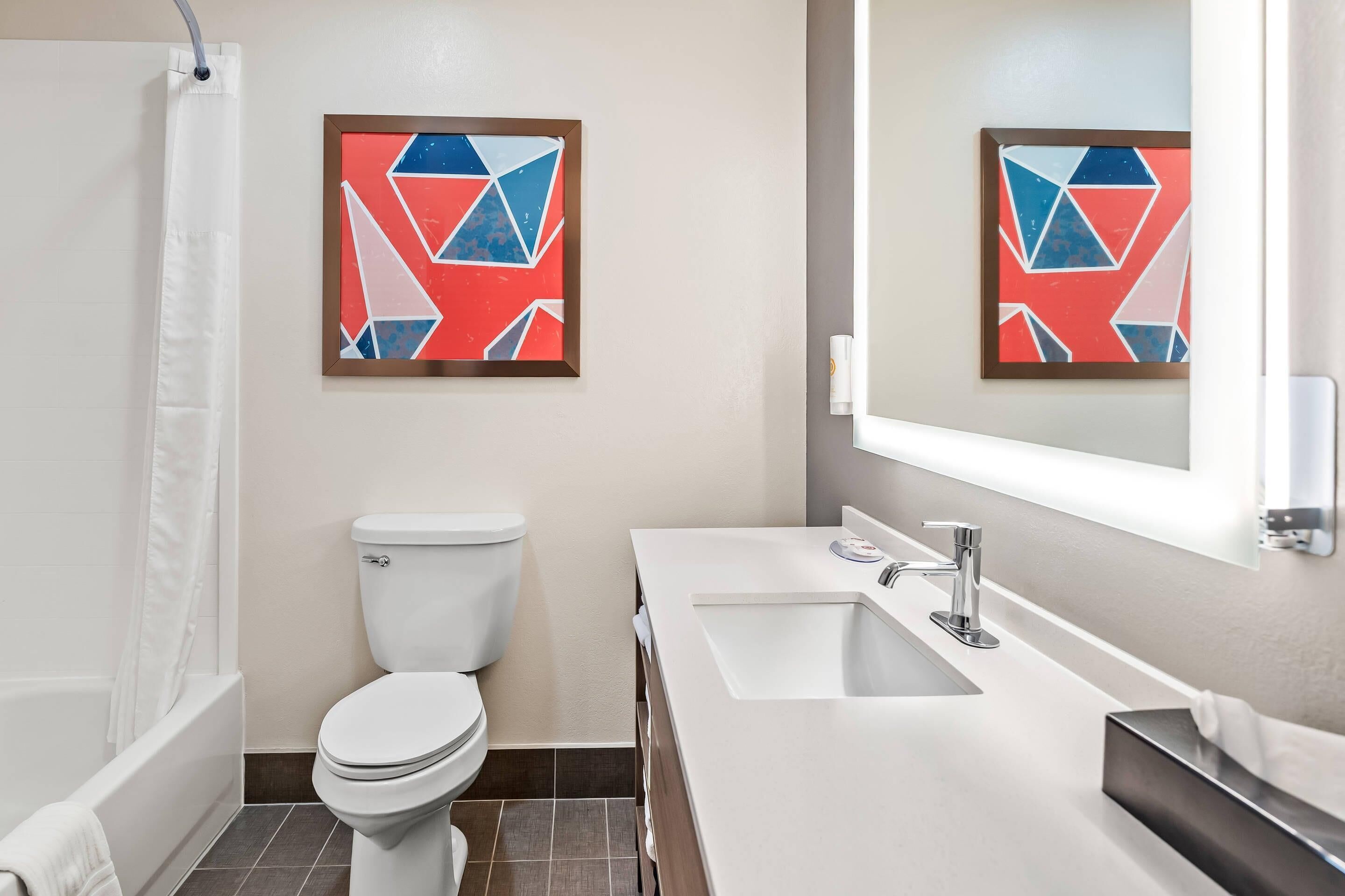 A modern bathroom with a toilet, sink, and shower. There are two framed artworks on the wall.