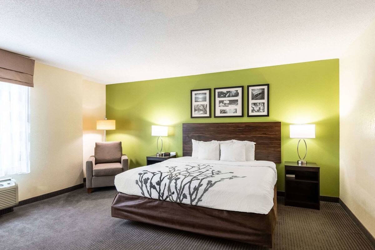 A hotel room with a bed, two bedside lamps, a chair, and a wall with framed pictures.