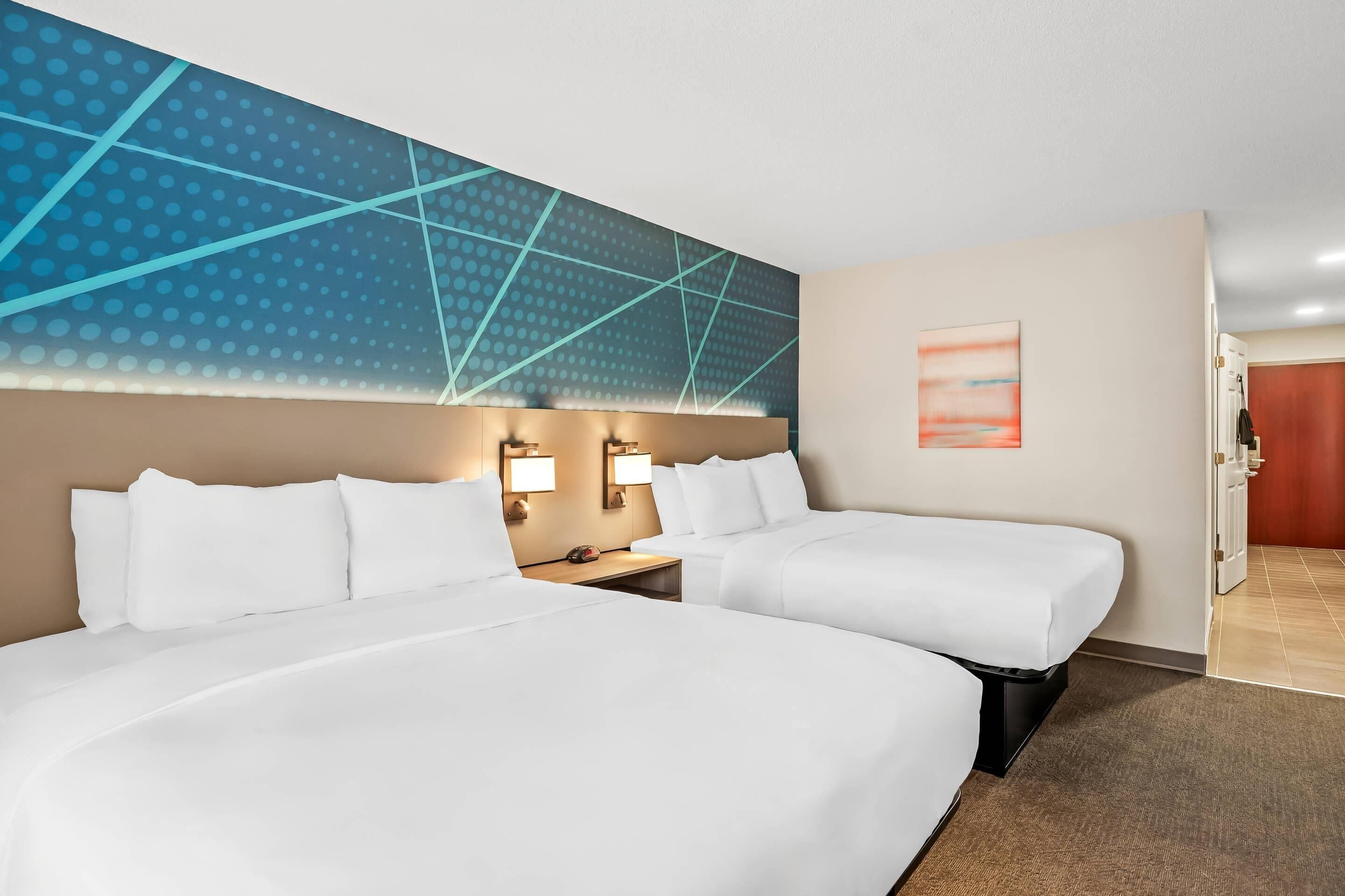 A hotel room with two beds, a large wall mural, and a painting.