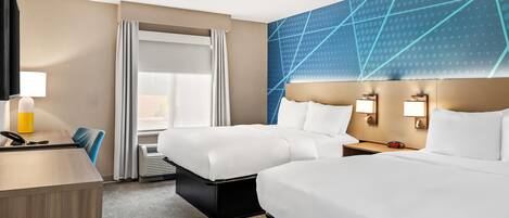 A hotel room with two beds, a desk, a chair, a TV, and a large wall with geometric patterns.