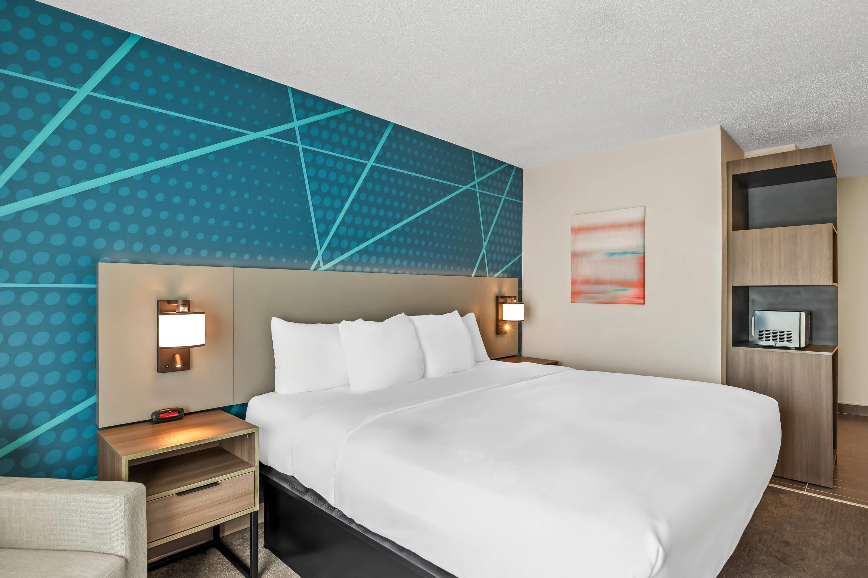 A hotel room with a large bed, two bedside tables with lamps, a wall-mounted TV, and a built-in shelving unit.