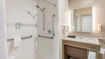 A modern bathroom with a shower, grab bars, a toilet, and a sink with a mirror.