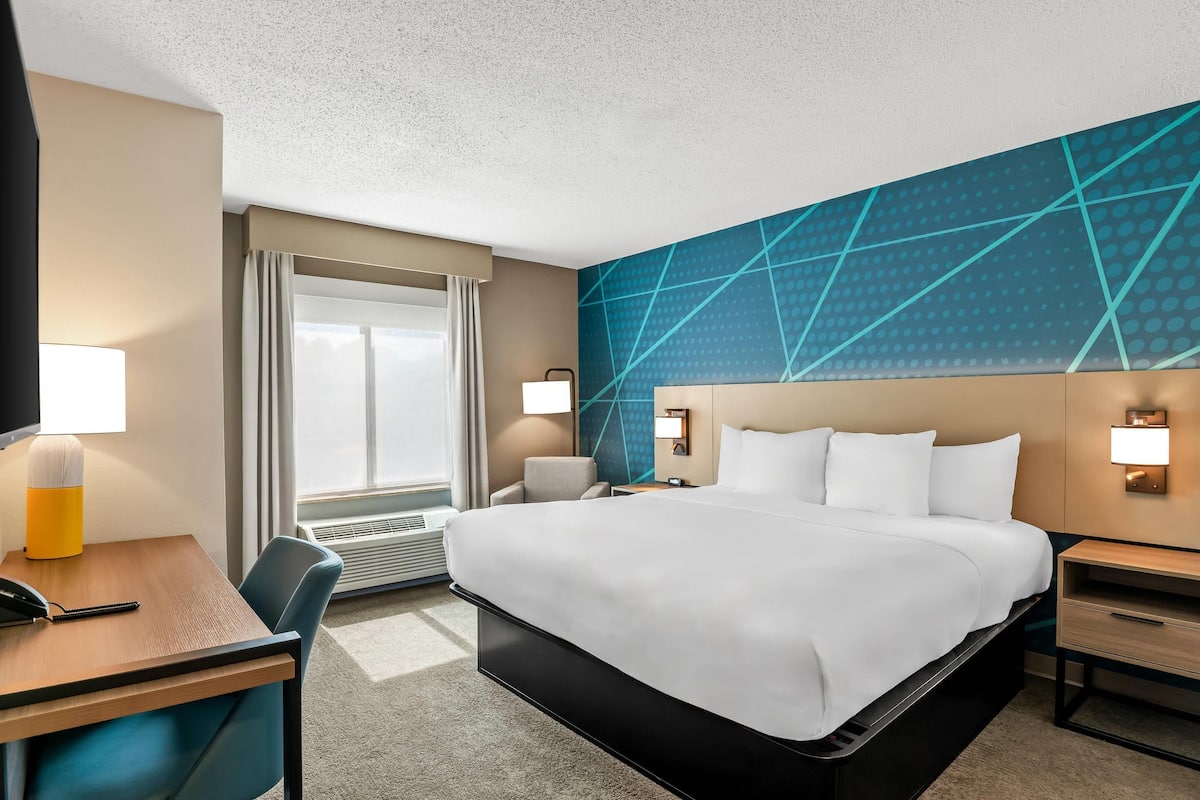 A hotel room with a large bed, a desk with a telephone, a chair, and a desk lamp.