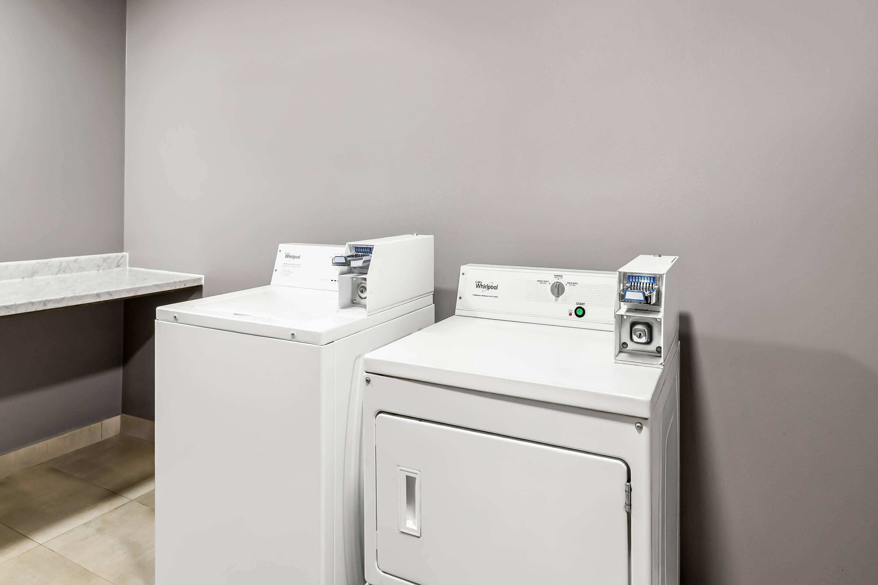 A laundry area with two white Whirlpool washers and a countertop.