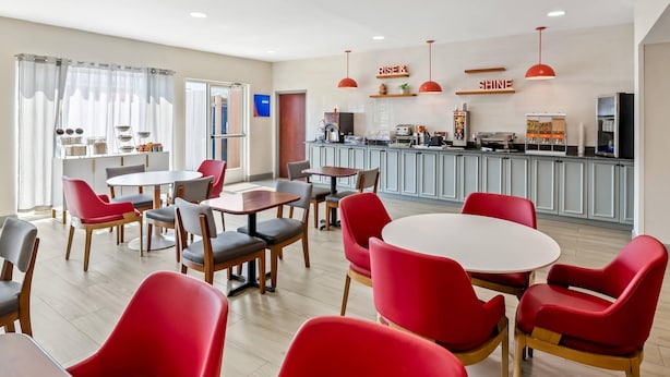 A modern dining area with red chairs and tables, a kitchen in the background, and a sign that reads "RISE & SHINE". - Comfort Inn Emporia (Emporia)