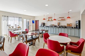 A modern dining area with red chairs and tables, a kitchen in the background, and a sign that reads "RISE & SHINE". - Comfort Inn Emporia (Emporia)