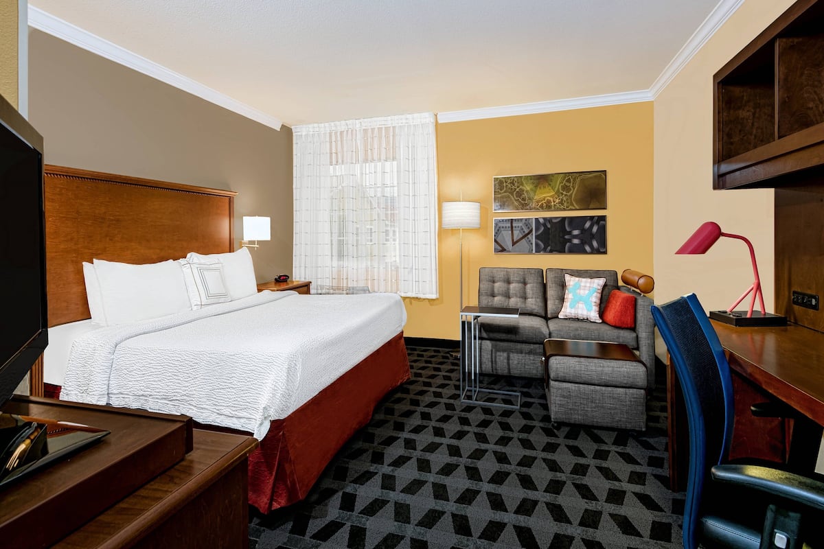 A hotel room with a large bed, a sofa, a desk, and a TV.