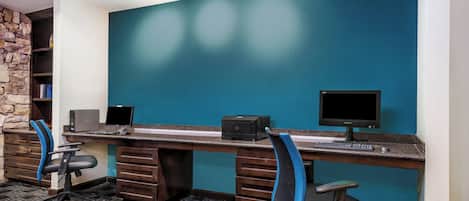 Ein moderner Arbeitsraum mit einer Wand in Türkis und einer Wand aus Stein, einem Schreibtisch mit Computer sowie zwei Bürostühlen.