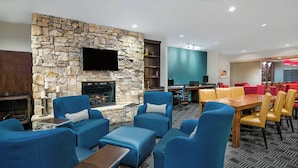 Un área lounge moderna con sofás azules, una chimenea de piedra, un televisor de pantalla plana y un comedor con sillas amarillas.