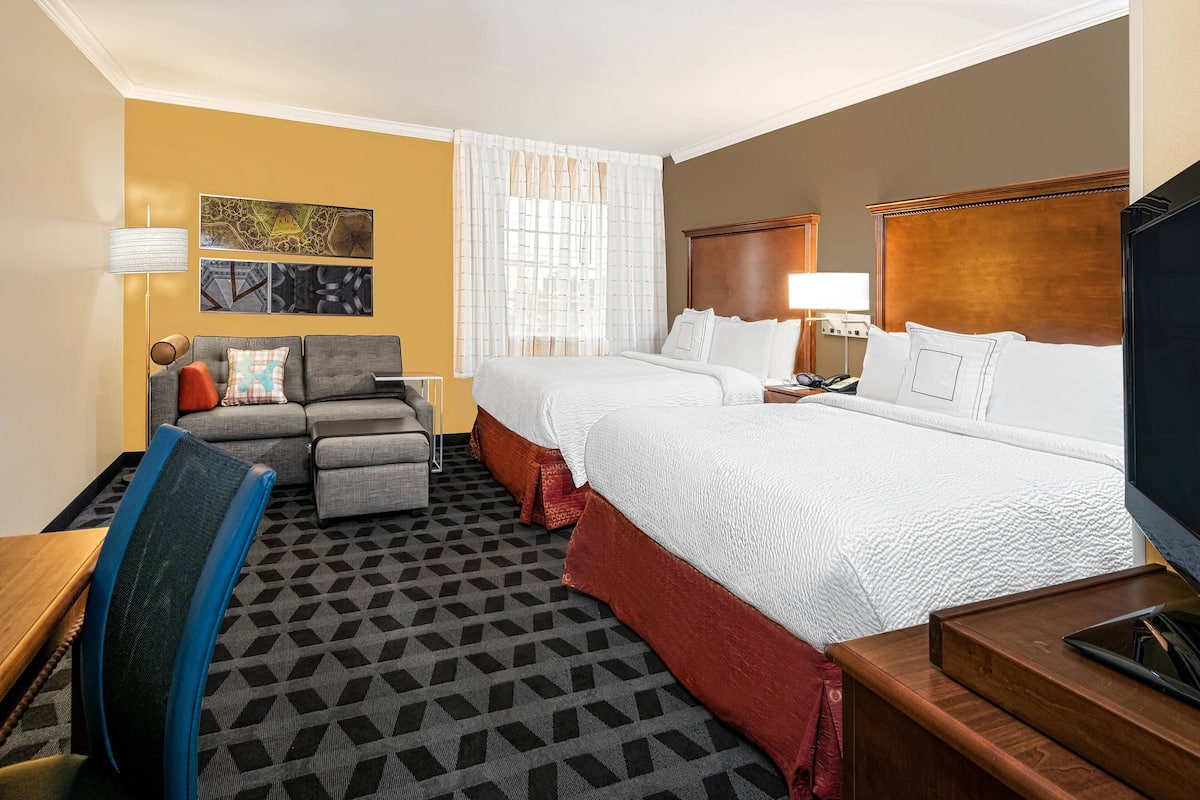 A hotel room with two beds, a sofa, a desk, and a TV.