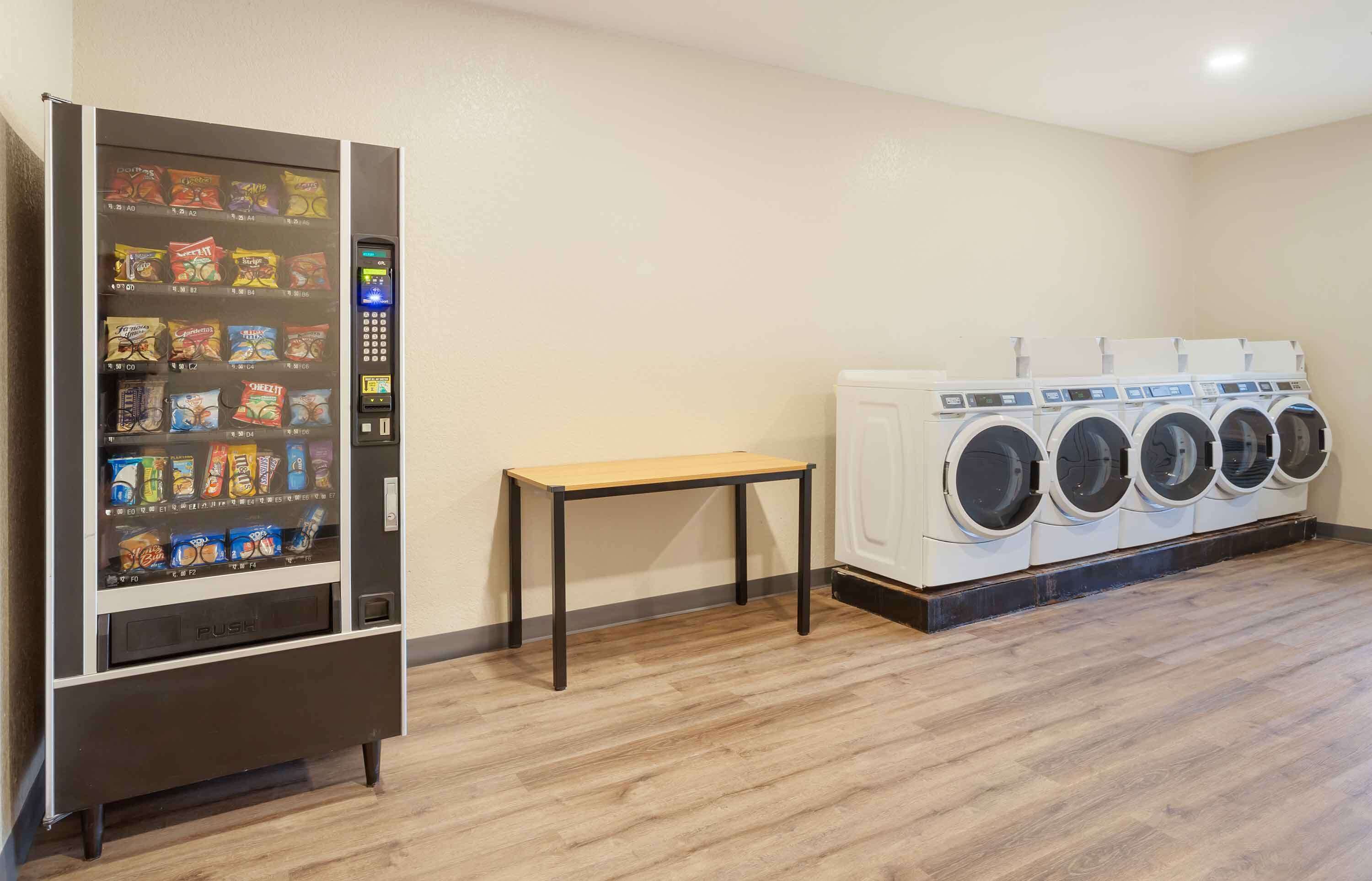 A laundry room with a vending machine, a table, and multiple washing machines.