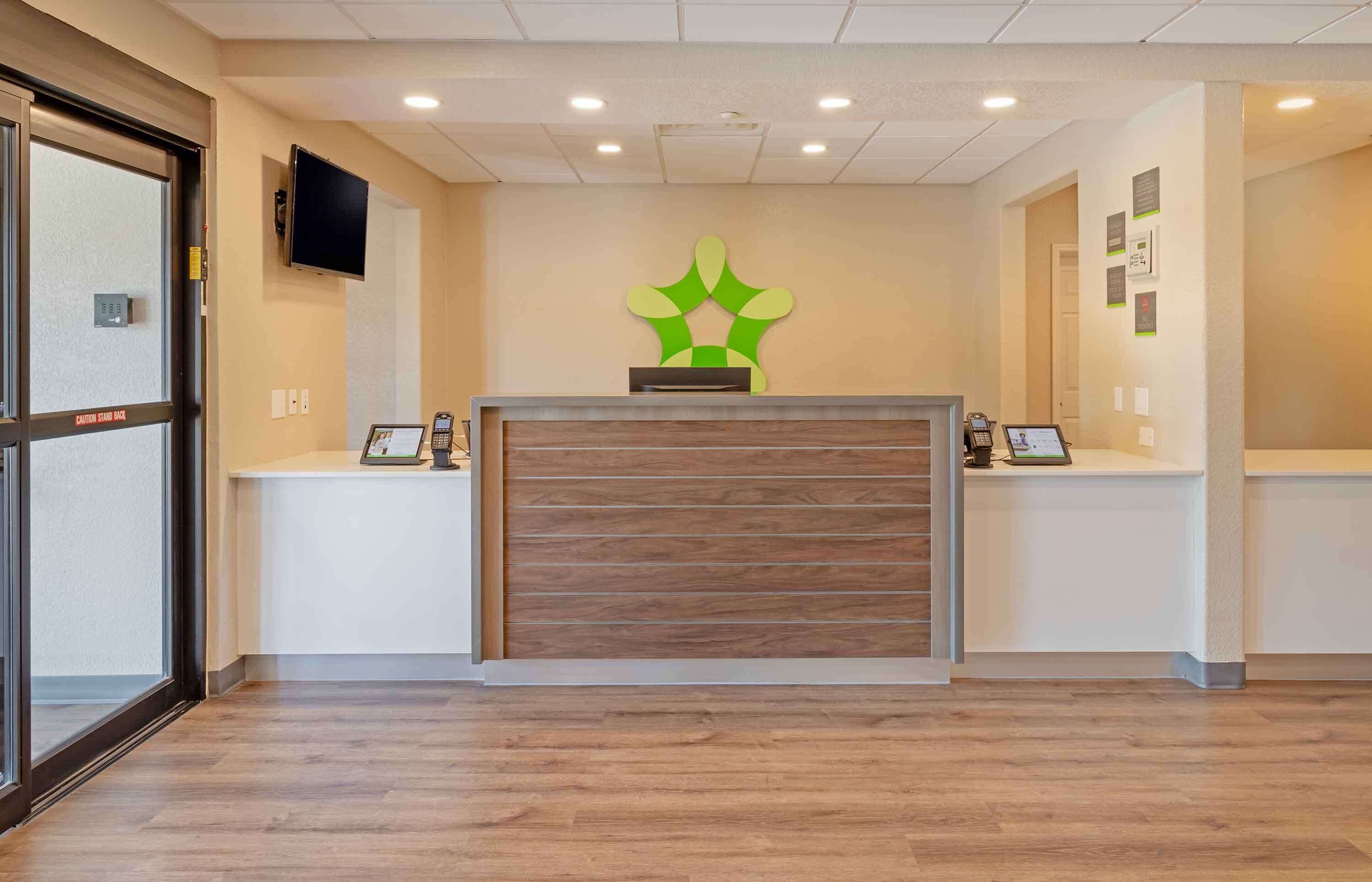 A reception area with a wooden reception desk, a mounted television, and a green wall decoration.