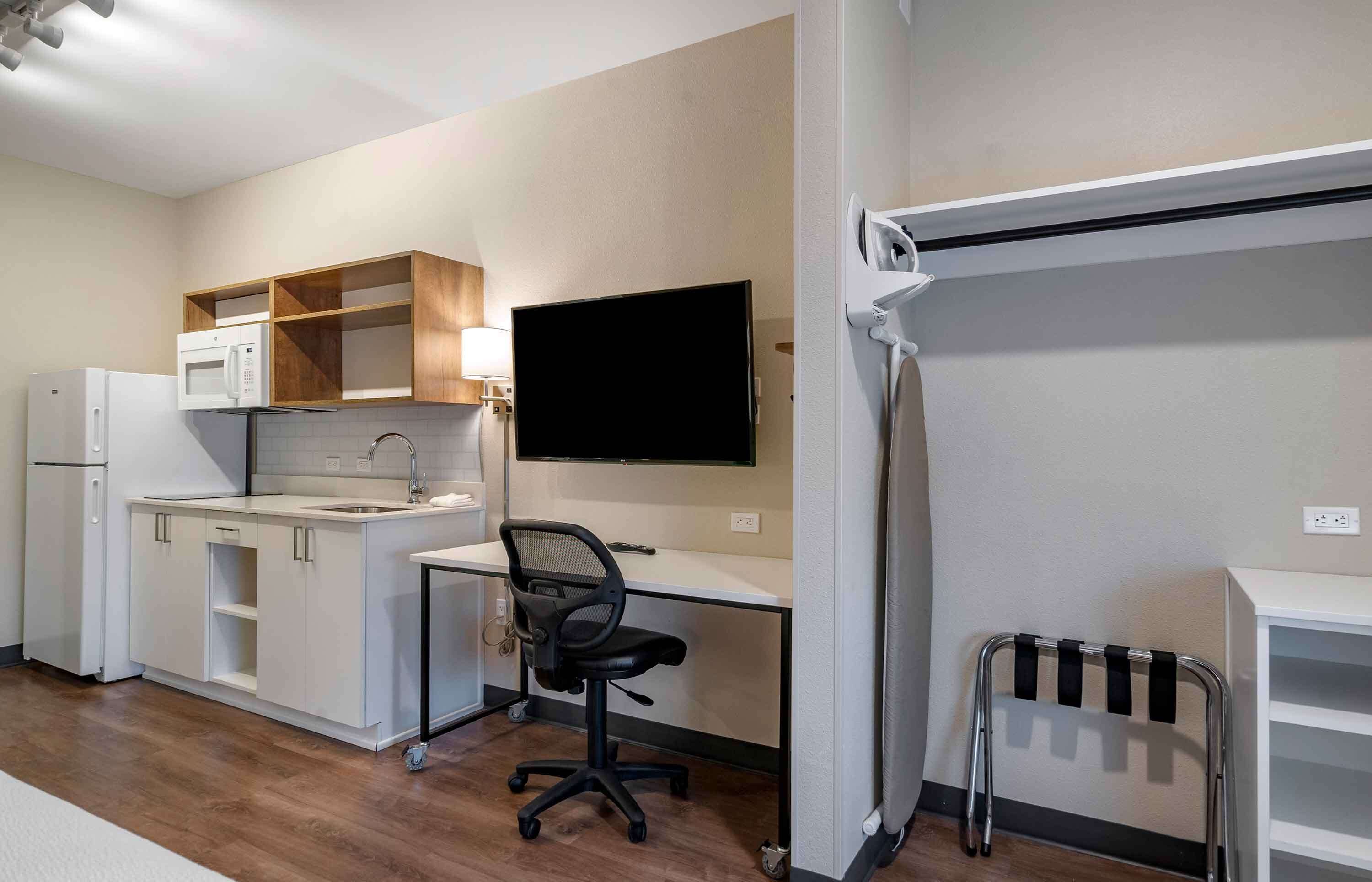A compact kitchenette with a microwave, refrigerator, and sink. There's a desk with a chair and a flat-screen TV mounted on the wall.