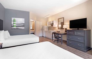 Une chambre d’hôtel avec deux lits, un bureau, une télévision, un miroir et une kitchenette.