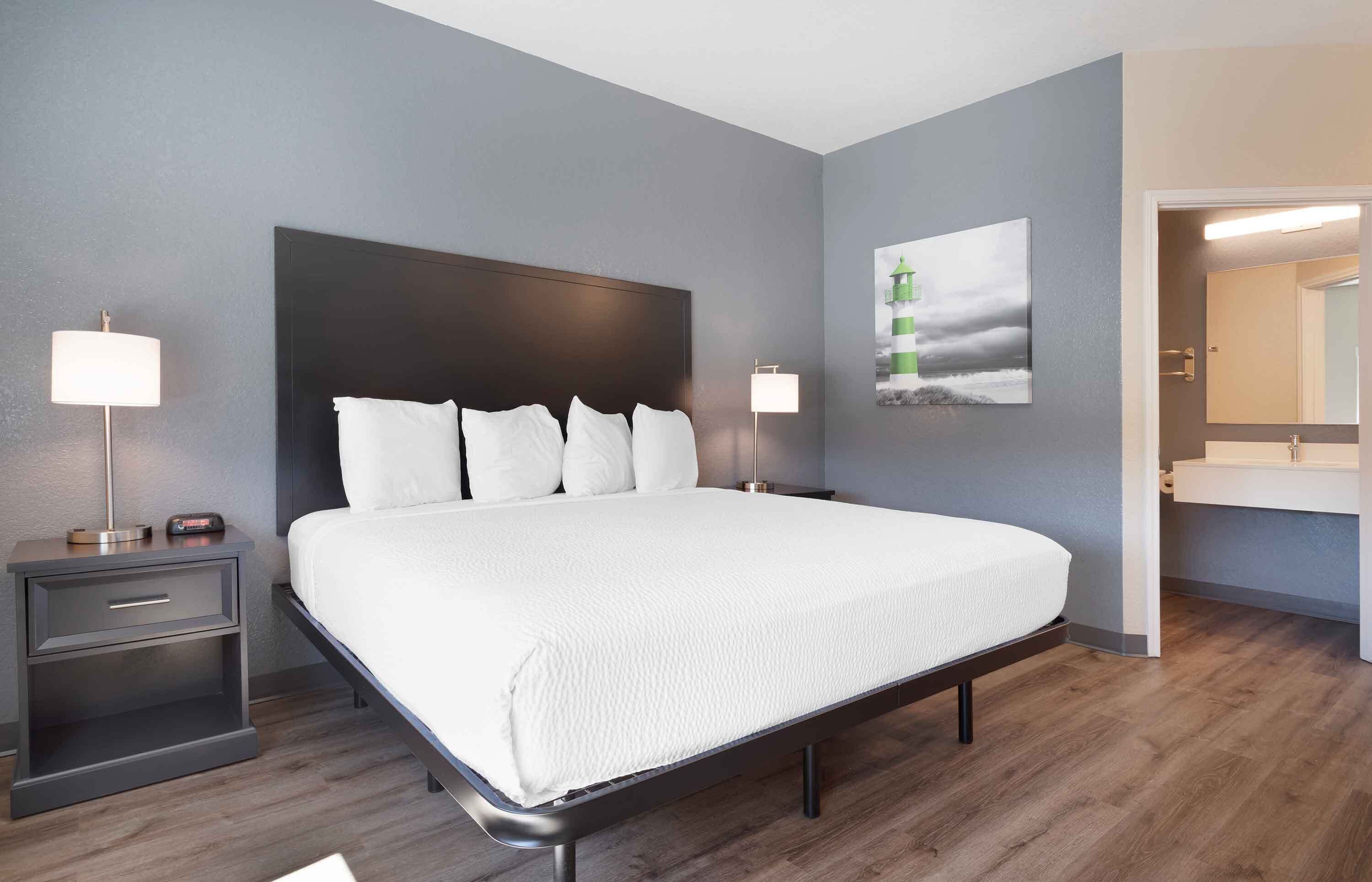 A modern hotel room with a large bed, bedside tables, a nightstand, a wall-mounted lamp, and a painting.