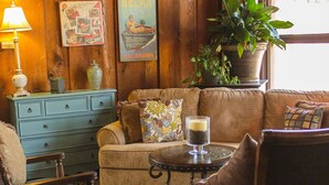A cozy living room with a blue dresser, a brown sofa, a coffee table, and a potted plant. - Charles Wesley Motor Lodge (Broken Bow)