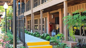 A building with a covered outdoor area, steps leading to a door, and a garden with various plants. - Charles Wesley Motor Lodge (Broken Bow)
