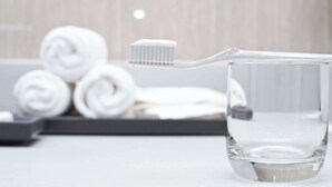 A clear glass cup with a toothbrush and rolled towels in the background. - Charles Wesley Motor Lodge (Broken Bow)