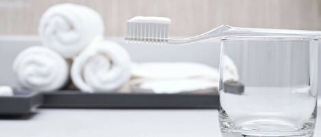 Un verre transparent contenant une brosse à dents, avec des serviettes enroulées en arrière-plan.
