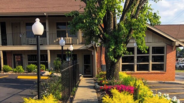 A two-story building with a covered front porch, a sidewalk, and a parking lot. - Charles Wesley Motor Lodge (Broken Bow)