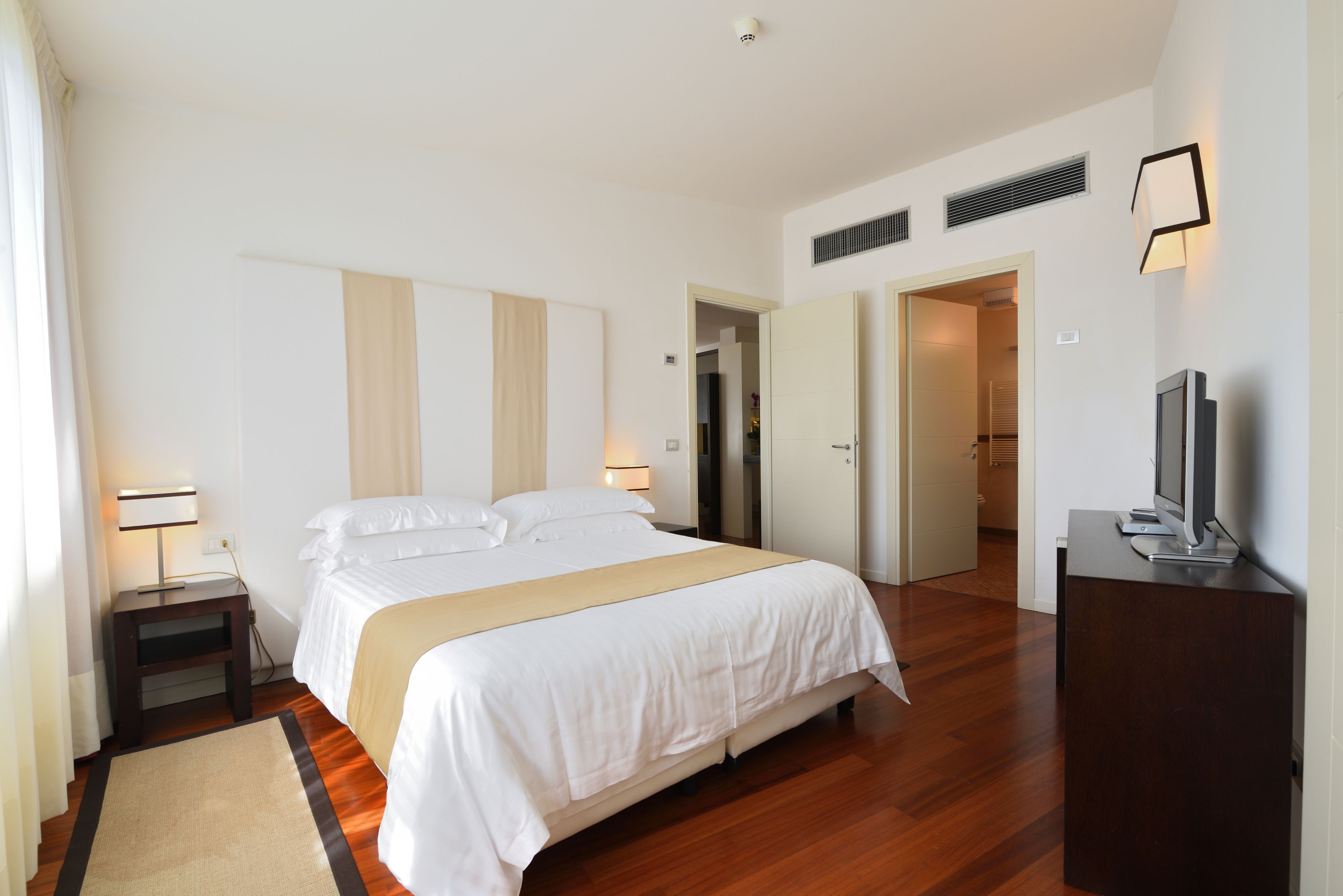 A hotel room with a large bed, bedside tables, a TV, and a wardrobe.