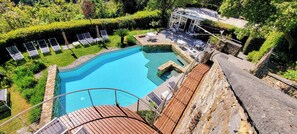 Piscina con sillones de descanso, terraza de piedra y vista a un edificio con área de estar al aire libre.
