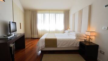 A hotel room with a bed, a desk with a computer, a lamp, and a window with curtains.