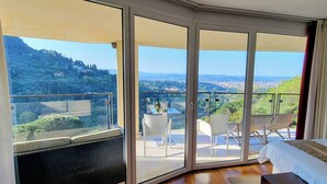 Une chambre d’hôtel dotée d’une grande porte-fenêtre coulissante donnant sur un balcon avec une table, des chaises et une vue sur un paysage montagneux.