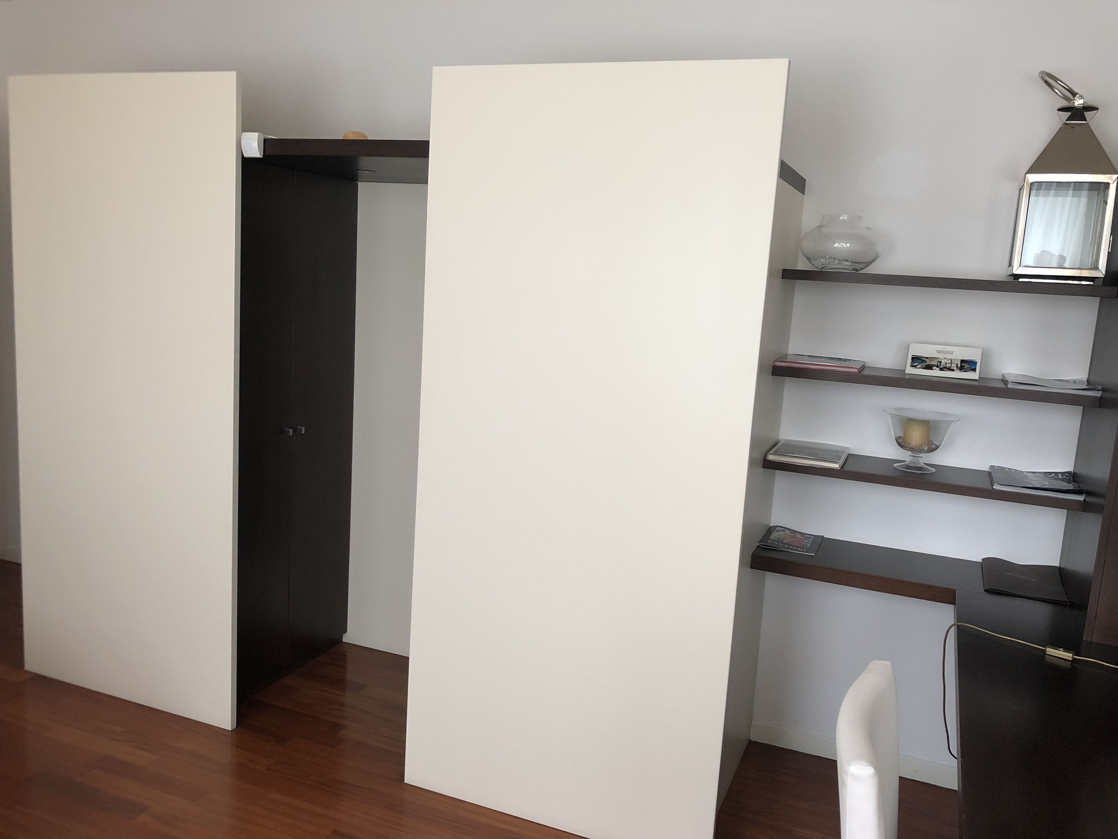 Ein modernes Zimmer mit Holzboden, einer weißen Trennwand, einer dunklen Tür und einem Regal mit Dekorationen.