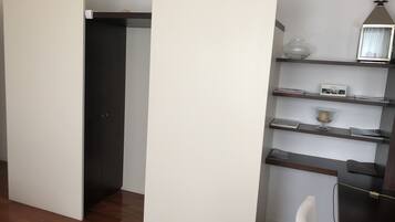Ein modernes Zimmer mit Holzboden, einer weißen Trennwand, einer dunklen Tür und einem Regal mit Dekorationen.