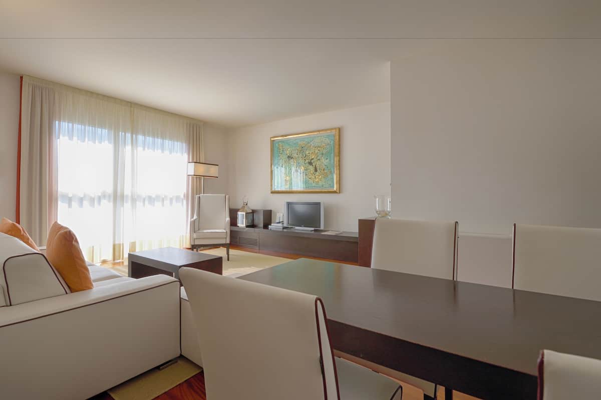Una habitación de hotel moderna con comedor, sofá, televisor y un cuadro en la pared.