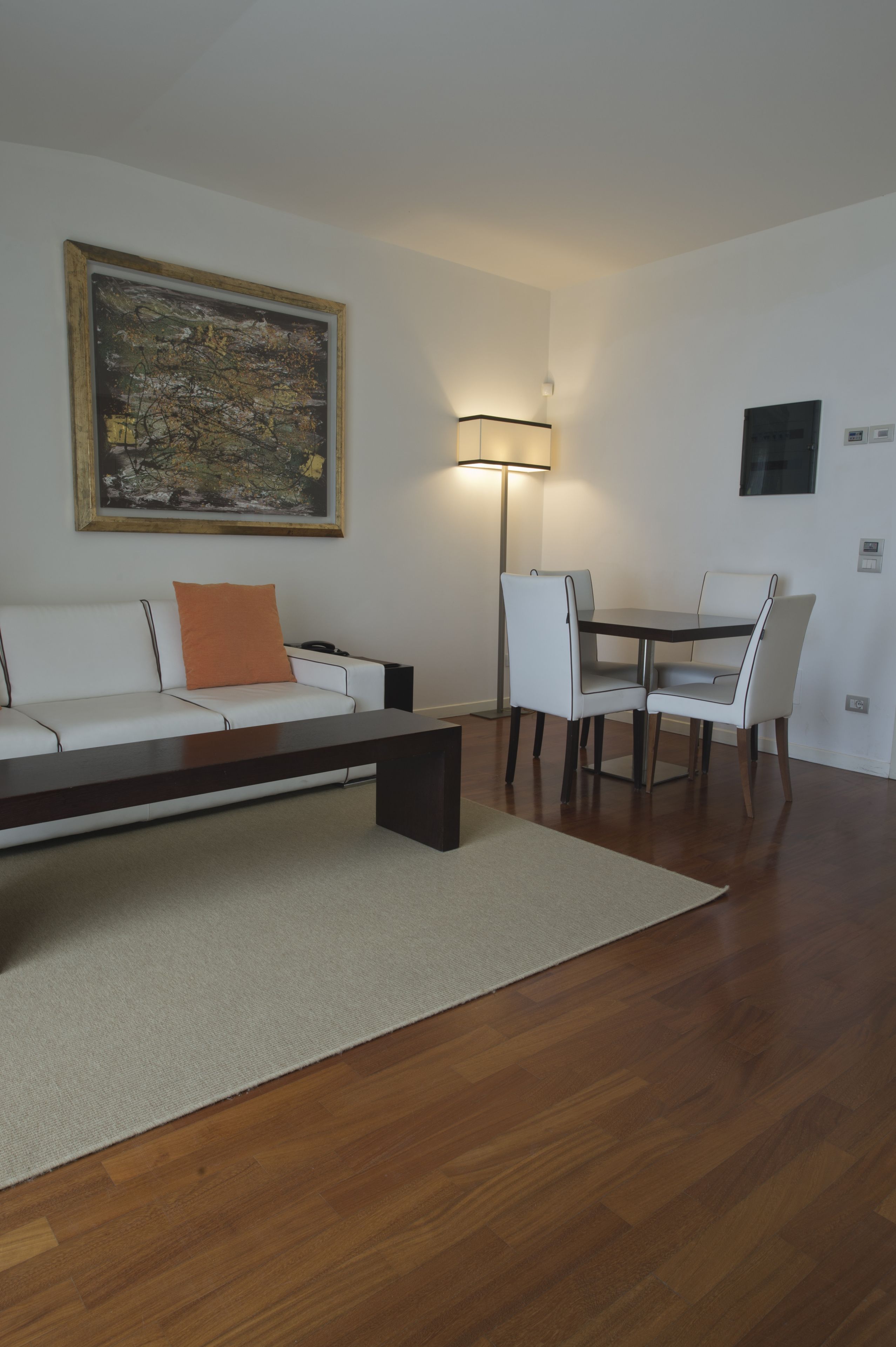 A modern living room with a sofa, a coffee table, a dining table with chairs, a floor lamp, and a painting on the wall.
