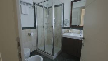 A modern bathroom with a glass-enclosed shower, a toilet, and a sink with a mirror.