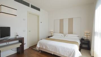 A hotel room with a bed, bedside tables, a desk, a television, and a window with curtains.