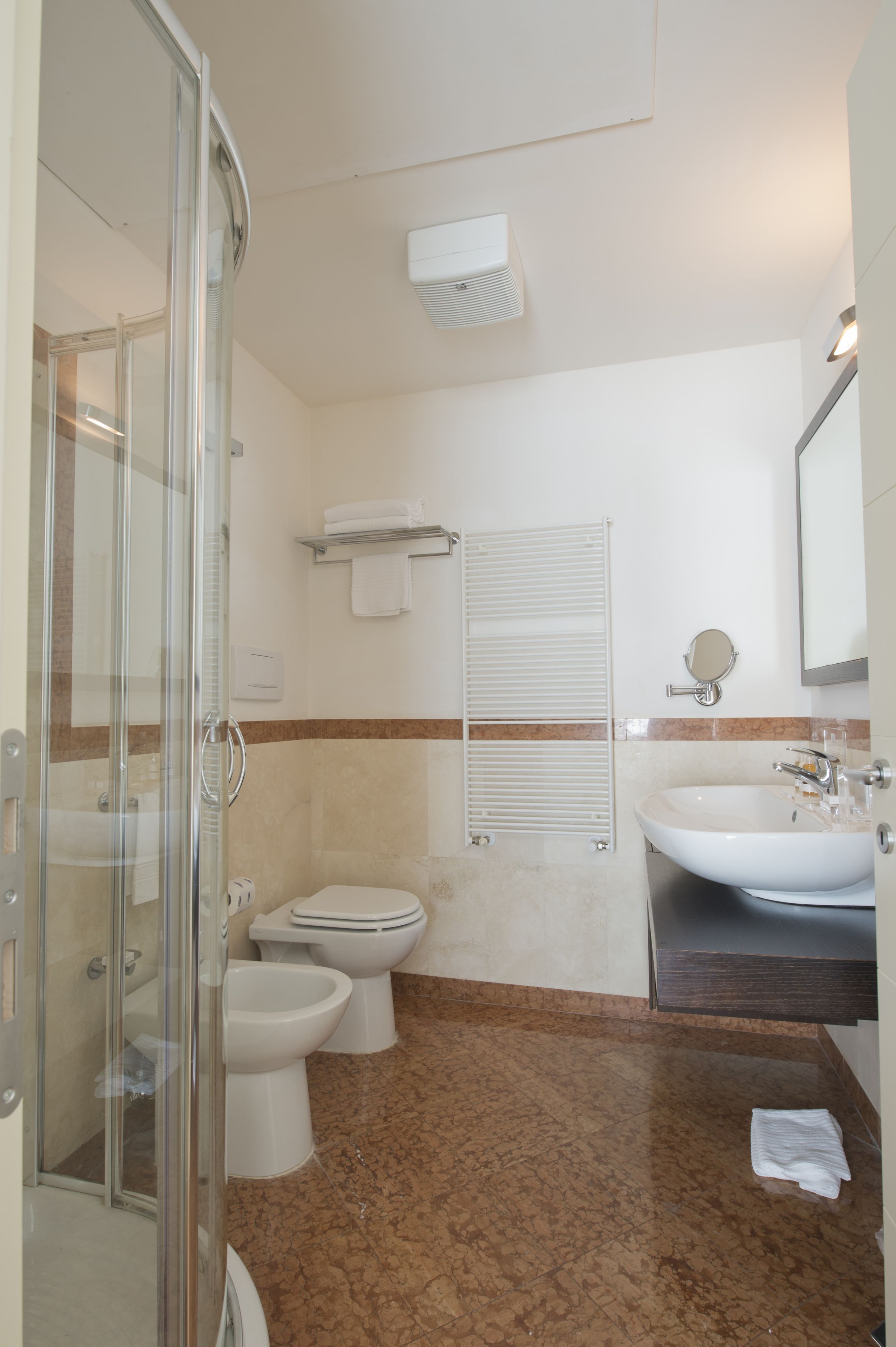 A bathroom with a glass shower enclosure, a toilet, bidet, and a sink.