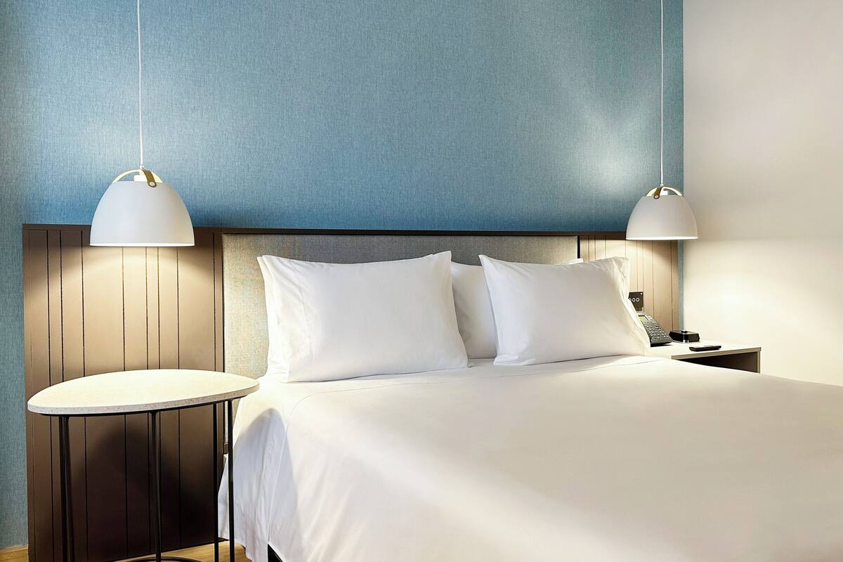 A neatly made bed with white linens and two pillows, flanked by two bedside tables with lamps, against a textured blue wall.
