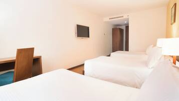 A hotel room with two beds, a desk, a chair, a TV, and a door leading to another room.