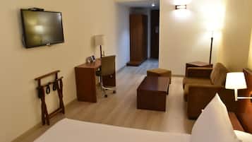Una habitación de hotel con cama, escritorio, sillón, sofá y televisor fijado a la pared.