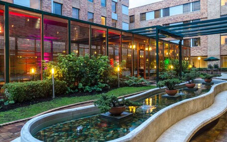 A modern building with a glass facade, a landscaped garden with a water feature, and outdoor seating areas.