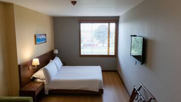Una habitación de hotel con una cama, una mesita de noche, una lámpara, un televisor y una ventana con persianas.